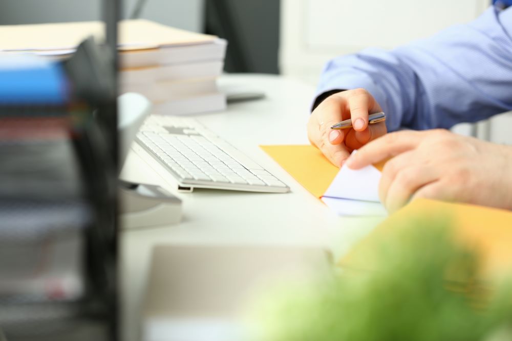 Close up of a businessman stuffing an envelope at a desk signifying the necessity of a postage meter.