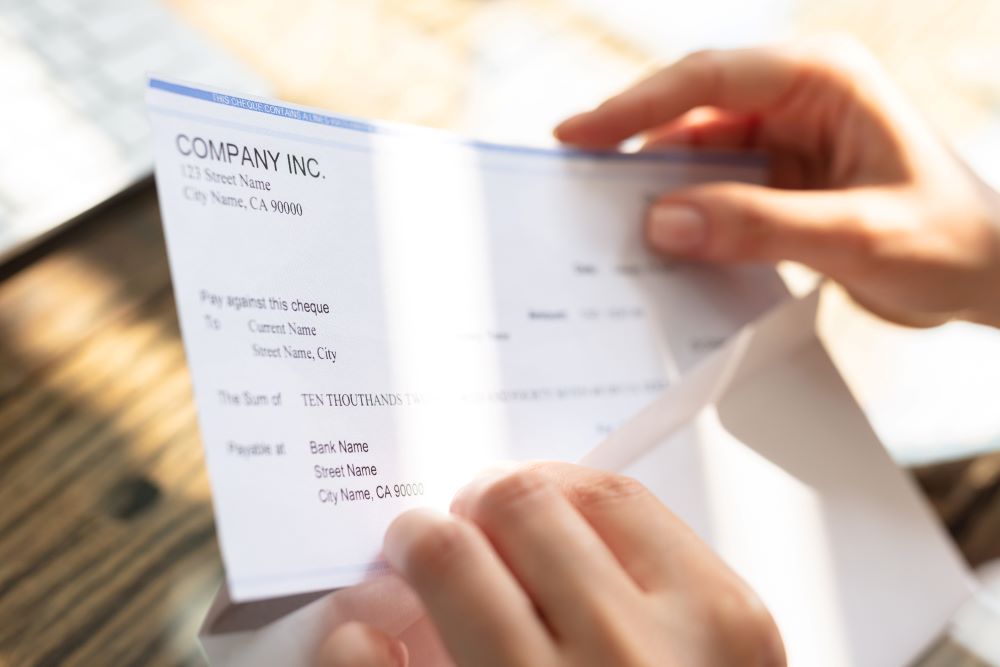 A person's hands are shown holding a business check from 'COMPANY INC.' in a sunlit setting, a transaction that could typically be processed with the assistance of a postage meter for mailing purposes.
